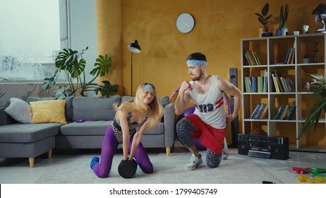 Freak Sports Couple From 80s. Vigorous Retro Fitness Girl Struggling To Lift Up Heavy Dumbbells. Her Lazy And Tricky Boyfriend Dancing Having Fun With Light Dumbbells.