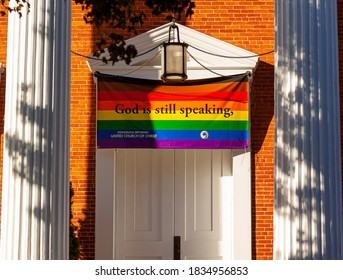 Frederick, MD, USA 10/13/2020: Close up image of the front door of the Evangelical Reformed United Church of Christ with a large LGBT flag that says God is still speaking. A welcoming progressive act.
