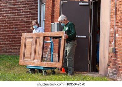 Frederick, MD, USA 10/14/2020: A Couple Wearing Face Mask Due To COVID-19 Are Replacing A Door In Their Shop. They Loaded The Door On A Platform Truck And Are Rolling It From Backdoor. A DIY Project.