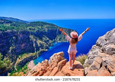 Free carefree joyful girl traveler with open arms stands on hill rock over sea bay in Turkey, butterfly valley. Enjoy travel concept 