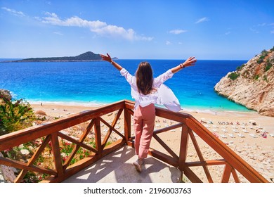 Free Carefree Traveler Girl Stands Alone With Open Arms On Stairs Against Backdrop Of Bay With The Turquoise Sea In Kas, Turkey