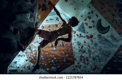 Free climber young man climbing artificial boulder indoors. Climbing concept and extreme activity. The young fit man on rock - Powered by Shutterstock