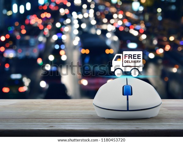 Free delivery truck\
flat icon with wireless computer mouse on wooden table over blur\
colorful night light city with cars in city, Business free delivery\
online concept