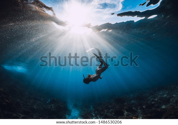 Free diver woman with fins\
over coral bottom and amazing sun rays. Freediving underwater in\
ocean