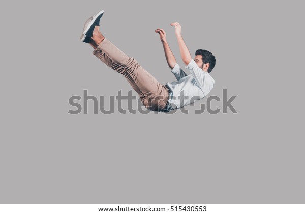 Free falling. Mid-air shot of handsome young\
man falling against grey background\
