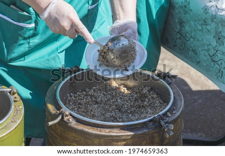 Free food distribution  A woman in a green apron puts buckwheat porridge on a plate from an army thermos