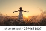 Free girl runs happily through meadow in grass in rays of sunset. Concept of female dreams, success, travel, flight. Young woman holding her arms to sides runs across field in sun. Happy running girl