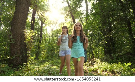 free girls travelers with backpacks go through the thicket in the forest. children tourists travel in summer park. teenagers looking for adventure. woman hiker. teamwork tourists