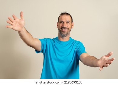 Free Hugs For The Person Who Had A Bad Day. Cheerful Friendly Latin Male Model In Blue T-shirt, Pulling Hands Towards Camera, Wanting To Hug, Smiling Broadly, Welcoming Friend To Come Into His Arms.