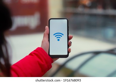 Free internet in the supermarket. Woman holds a mockup of a smartphone with an icon on a white screen against the background of the escalator in the mall - Powered by Shutterstock