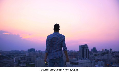 Free man standing on roof edge at dusk, desire to find strength and independence
