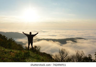 Free Man Standing On Top Of Mountain Over The Clouds At Sunrise. Man With Arms Raised  Looking At Beautiful Foggy Landscape On Hiking Trip. Blue Ridge Parkway Near Blowing Rock, North Carolina, USA.