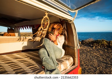 Free modern hippy female smile and enjoy roaming connection sending messages with mobile phone sitting inside an old classic vintage restored van. Travel vanlife digital nomad people - Powered by Shutterstock