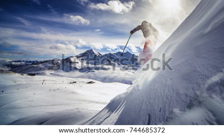 Free ride skier, skiing down steep slope, good background with blue skies and mountains
