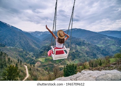 Free romantic woman traveler with open arms enjoying of swinging on heavenly swing and mountain view. Calm and quiet wanderlust concept moment when person feels happiness life and freedom