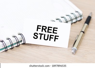 Free Stuff inscription on a white card on the table next to a notebook and a golden pen
