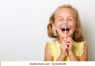 Free time for fun. Close up portrait of fancy, small girl with fake paper mustache cheerfully laughs isolated on grey background with copy space for text. - Powered by Shutterstock