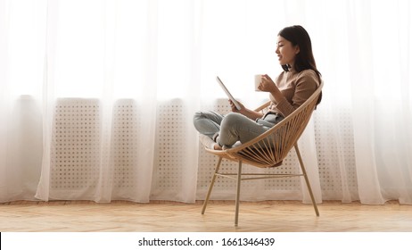 Free time. Girl using tablet and drinking coffee, sitting in wicker chair against window, panorama with free space - Shutterstock ID 1661346439