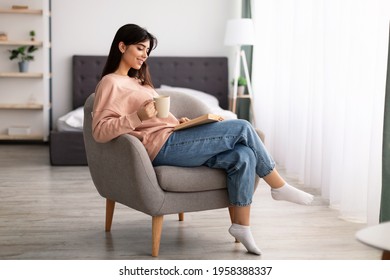 Free Time To Relax. Portrait of beautiful calm woman sitting on comfortable chair at home, reading paper book, holding cup and drinking hot coffee. Happy lady taking break from work, copy space - Powered by Shutterstock