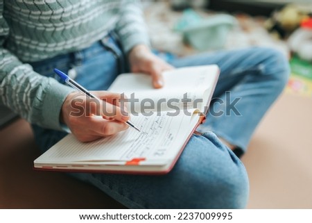 Free time you need to do something, woman unrecognizable sits on floor of room, in chair, writes in notebook. Lot of things have accumulated you need to write down in diary so as not to forget.