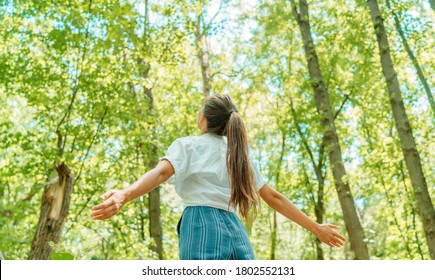 Free woman breathing clean air in nature forest. Happy girl from the back with open arms in happiness. Fresh outdoor woods, wellness healthy lifestyle concept.