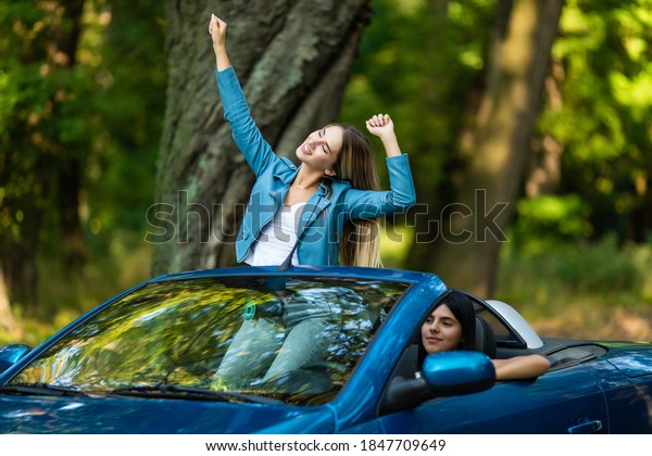 Free woman in cabriolet\
cheering joyful with arms raised. Woman going on road trip travel\
on summer day