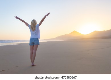 Free woman enjoying freedom feeling happy at beach at sunrise. Serene relaxing woman in pure happiness and elated enjoyment with arms raised outstretched up. 