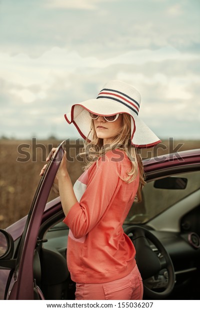 Free woman on car travel\
looking summer sunset sky. Girl driver leaning on car bonnet\
raising arms 