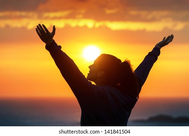 Free woman raising arms to golden sunset summer sky like praising. Freedom, success and hope concept. Girl relaxing and enjoying peace and serenity on beautiful nature.