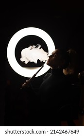 free woman smokes a hookah in the semi-darkness against the background of a ring lamp.