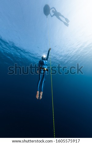 Freediver ascends along the rope from the depth while another freediver relaxes on the buoy