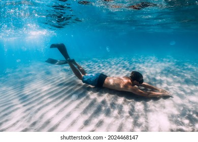 Freediver Male Glides Underwater Over Sandy Bottom In Blue Water. Swimming Underwater With Fins