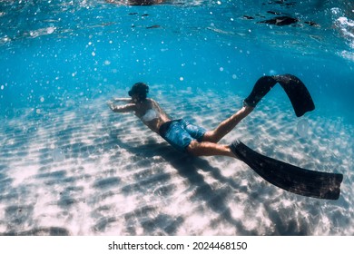 Freediver Male Glides Underwater Over Sandy Bottom In Blue Water. Swimming Underwater With Fins