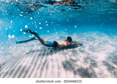 Freediver Male Glides Underwater Over Sandy Bottom In Blue Water. Swimming Underwater With Fins