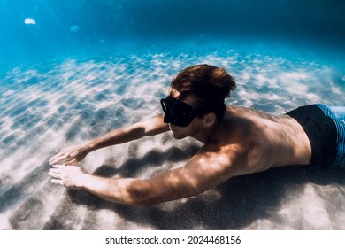 Freediver Male Glides Underwater Over Sandy Bottom In Blue Water. Swimming Underwater With Fins