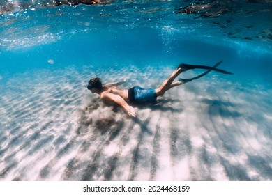 Freediver Male Glides Underwater Over Sandy Bottom In Blue Water. Swimming Underwater With Fins