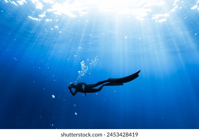 Freediver Swimming in Deep Sea With Sunrays. Young Man DIver Eploring Sea Life.