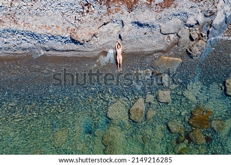 Freediver woman with fins posing on stony ocean coastline. Aerial view