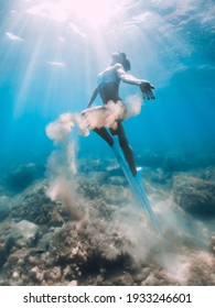 Freediver woman glides with sand in hand. Free diver with fins posing underwater