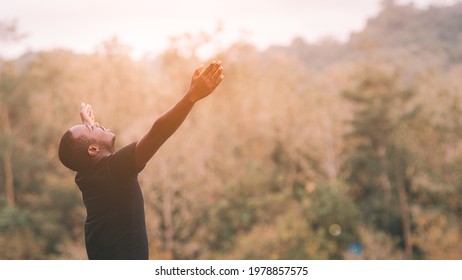 Freedom African Man Is Relaxing In Green Nature With Squint Eyes And Raised Up To Sky Arms At Sunny Summer Day. Emotion Feel Good And Travel Adventure Concept