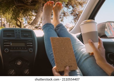 Freedom Car Travel Concept. Woman Relaxing With Feet On Dashboard. Girl With Drink And Book Looking The Tree.