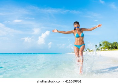 Freedom carefree girl playing splashing water having fun on tropical beach vacation getaway travel holiday destination. Playful woman with abs slim bikini body relaxing feeling free. 