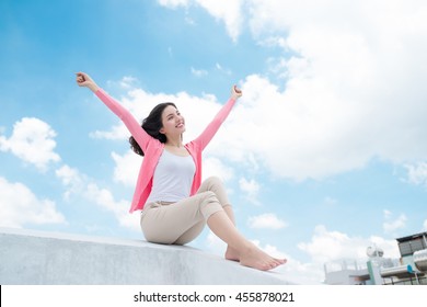 Freedom concept. Enjoyment. Asian young woman relaxing under blue sky on rooftop with her hands raised towards sky - Powered by Shutterstock