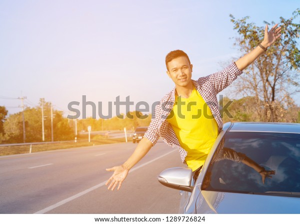 Freedom - enjoying road trip travel on summer day\
. Excited man raising his hand out of the car. traveling by car\
with joy in holiday