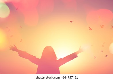 Freedom and feel good concept. Copy space of silhouette woman rising hands on sunset sky double exposure colorful bokeh light and birds fly background. Vintage tone filter effect color style.
