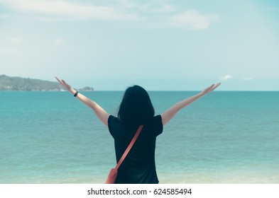 Freedom feel good and travel adventure concept. Copy space of silhouette woman rising hands with blue sky and white cloud on beach background. Vintage tone filter effect color style.