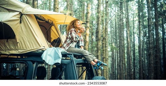 Freedom feeling and adventure lifestyle people. Traveler adult female chilling outside her car vehicle roof tent and enjoy nature sounds smiling. High trees forest green woods background. Scenic place