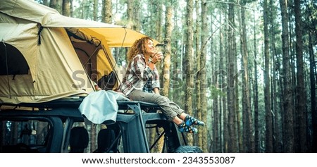Freedom feeling and adventure lifestyle people. Traveler adult female chilling outside her car vehicle roof tent and enjoy nature sounds smiling. High trees forest green woods background. Scenic place