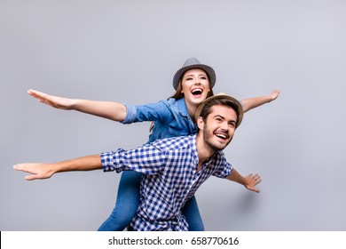 Freedom and fun, emotions and feelings. Cheerful and playful couple in casual outfits and hats are fooling around, gesturing plane wings, smiling, posing, going crazy on pure light background