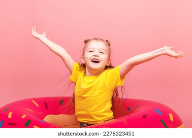 Freedom and happiness concept. Beautiful little happy girl with raising up her hands is sitting on a bright inflatable circle on pink background enjoy sunny day. Summer happy moment. - Powered by Shutterstock